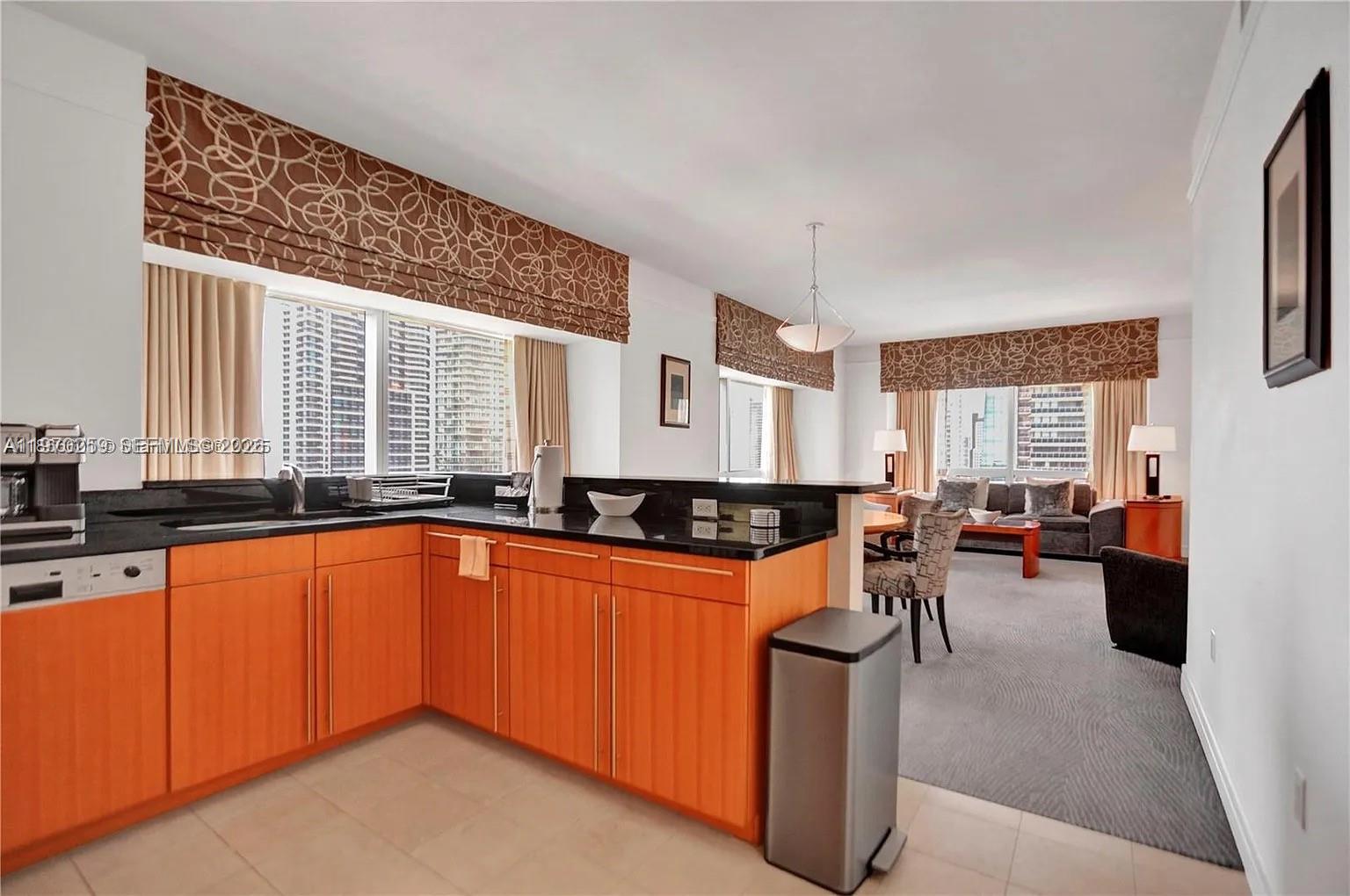 A kitchen with orange cabinets and black countertops opens into a carpeted living area — 1435 Brickell Ave # 3212, Miami FL 33131, MIAMI, FL