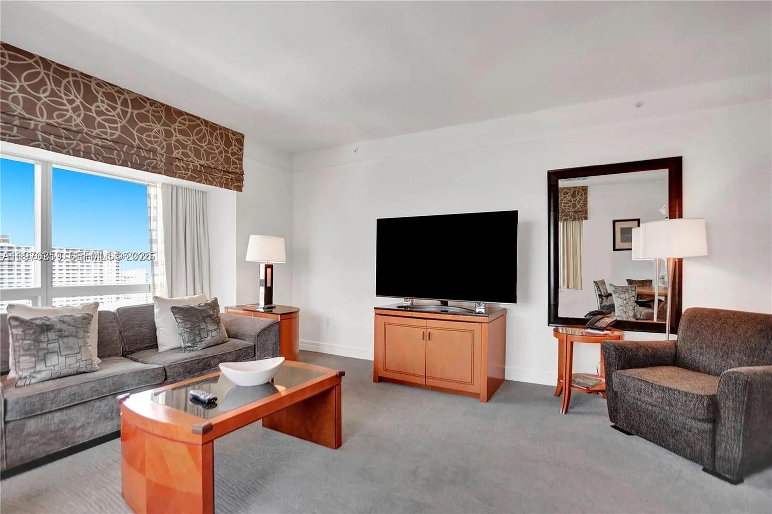A living room features a gray sofa, a television on a wooden console, and a mirror — 1435 Brickell Ave # 3212, Miami FL 33131, MIAMI, FL