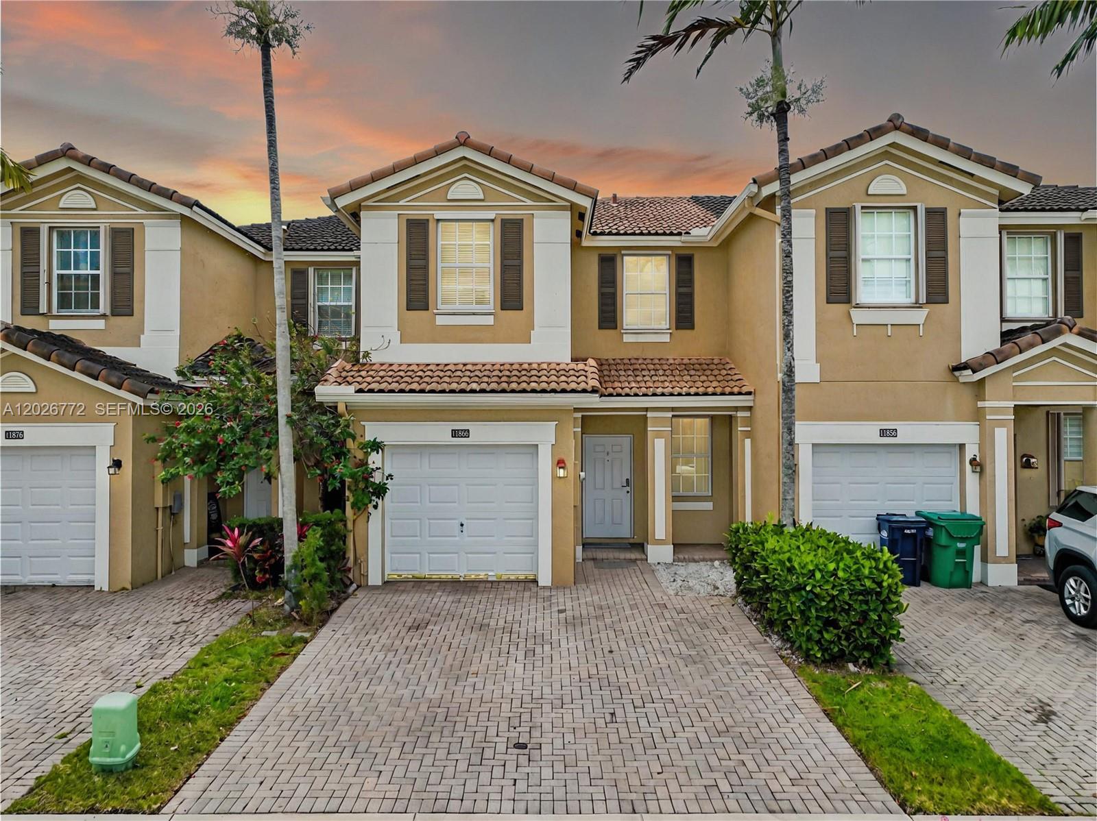 A row of three tan townhouses with tiled roofs and brick paver driveways at sunset — 11866 SW 152nd Pl, Miami FL 33196, MIAMI, FL