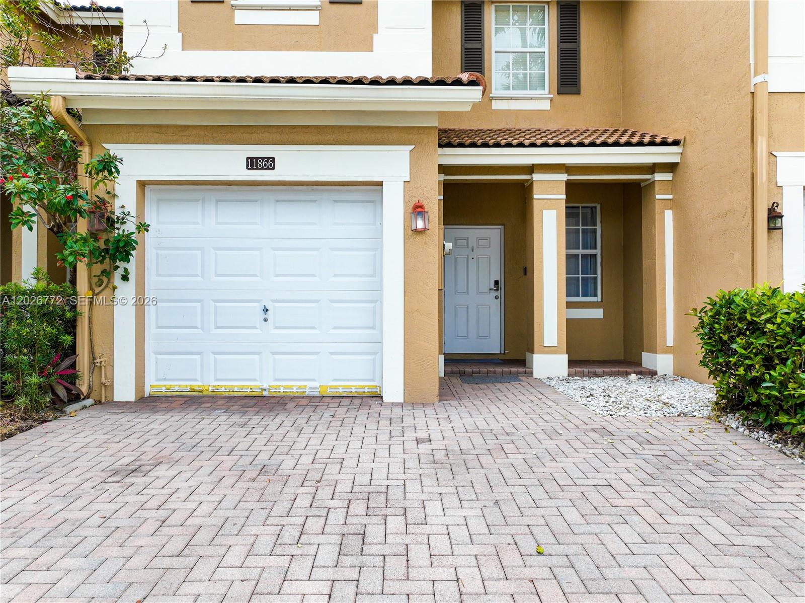 The exterior of a tan two-story house features a white garage door and front door — 11866 SW 152nd Pl, Miami FL 33196, MIAMI, FL