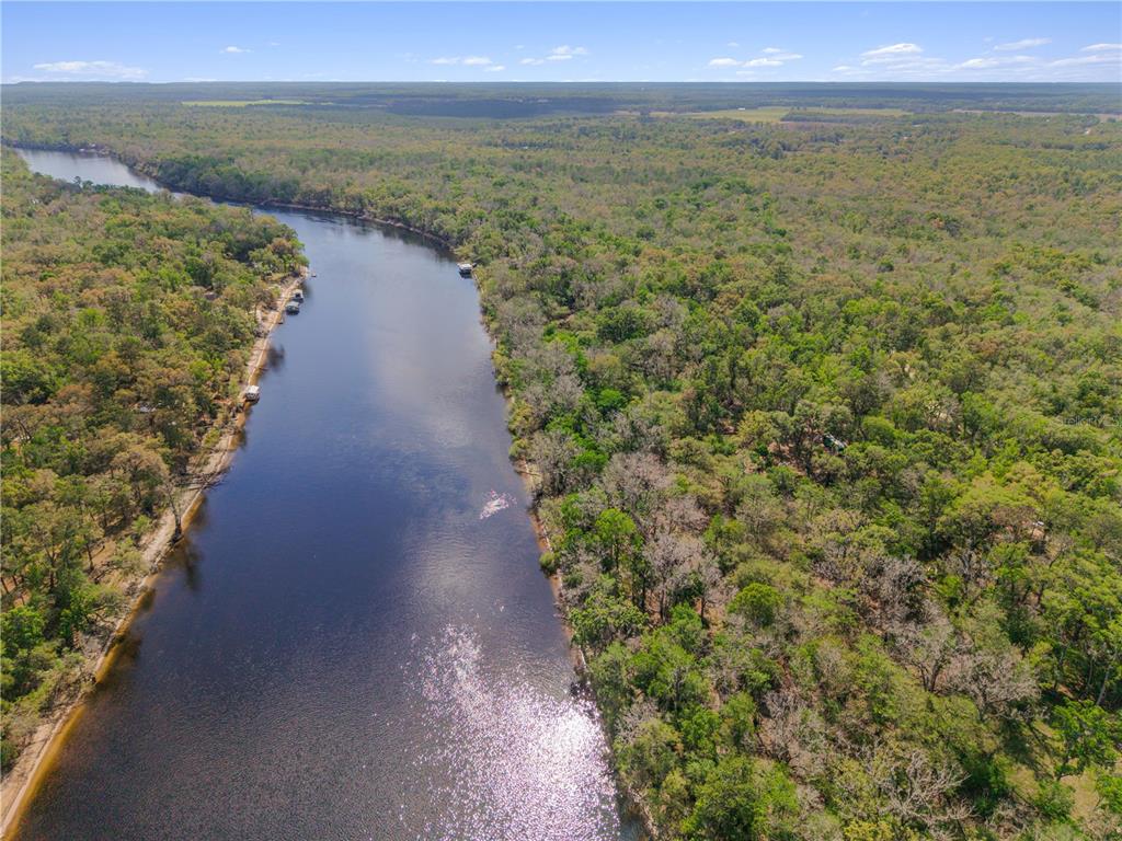 An aerial view shows a river winding through a dense forest with small boat docks — 615 NE 904 STREET, OLD TOWN, FL
