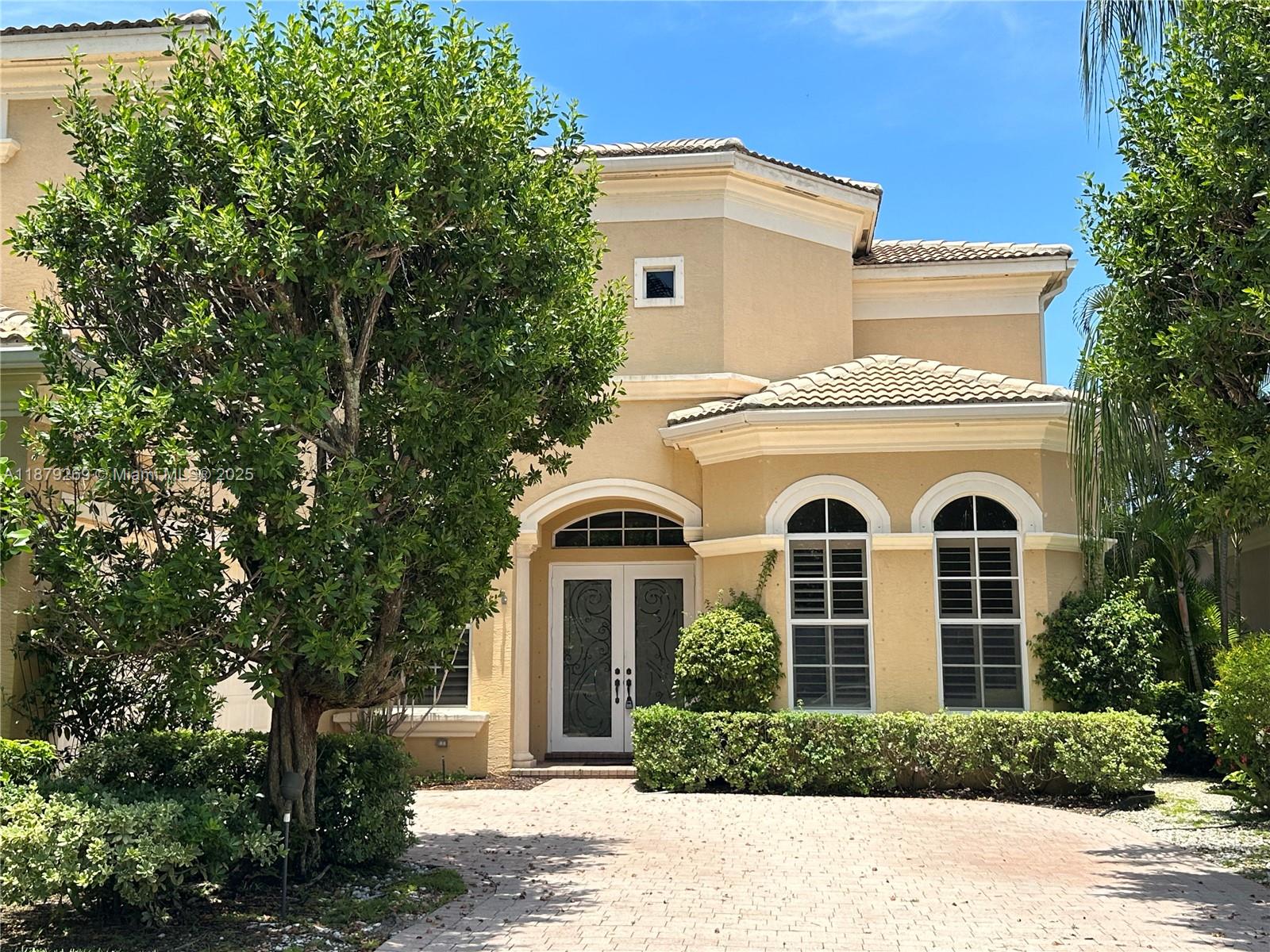 A two-story beige stucco house features a paved driveway, arched windows, and a double-door entrance — 138 Tranquilla Dr, Palm Beach Gardens FL 33418, PALM BEACH GARDENS, FL