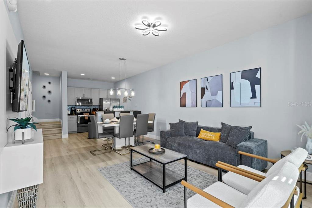 An open-concept living and dining area features light wood flooring, gray furniture, and modern lighting — 3212 OYSTER LANE, KISSIMMEE, FL