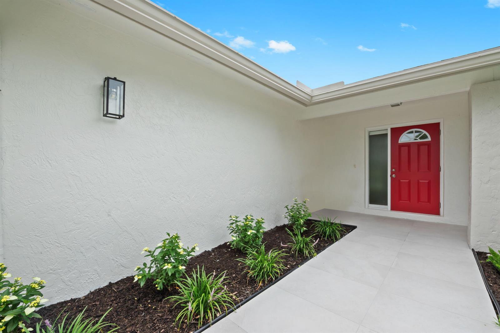 A red front door stands at the end of a tiled walkway beside a garden — 561 SW 168th Terrace, Weston FL 33326, WESTON, FL