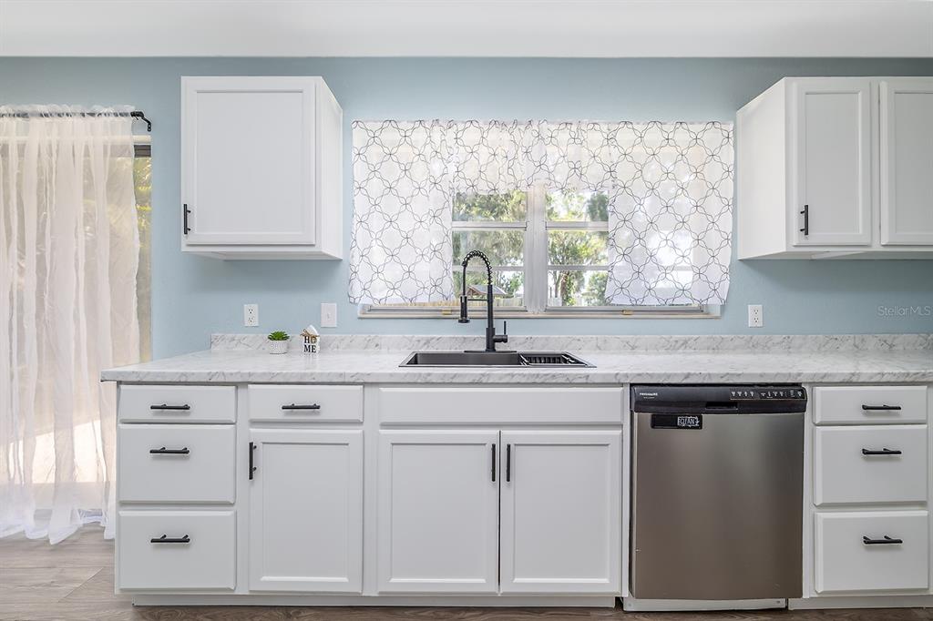 A kitchen features white cabinets, a marble-look countertop, a stainless steel dishwasher, and a window — 764 REED CANAL ROAD, SOUTH DAYTONA, FL