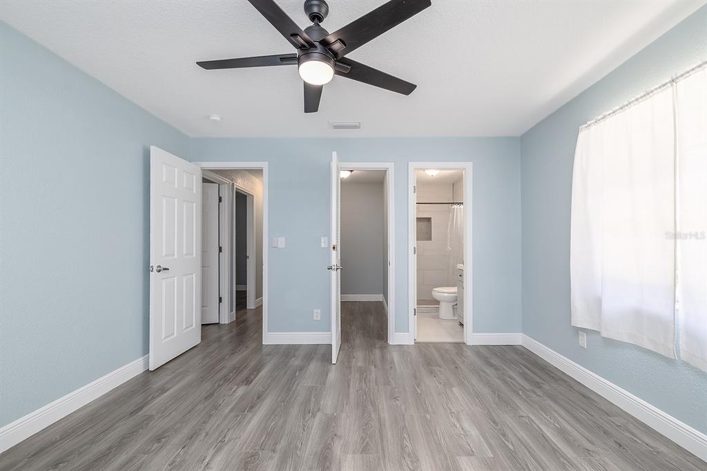 A bedroom with light blue walls, gray wood-look flooring, a ceiling fan, and three doorways — 764 REED CANAL ROAD, SOUTH DAYTONA, FL