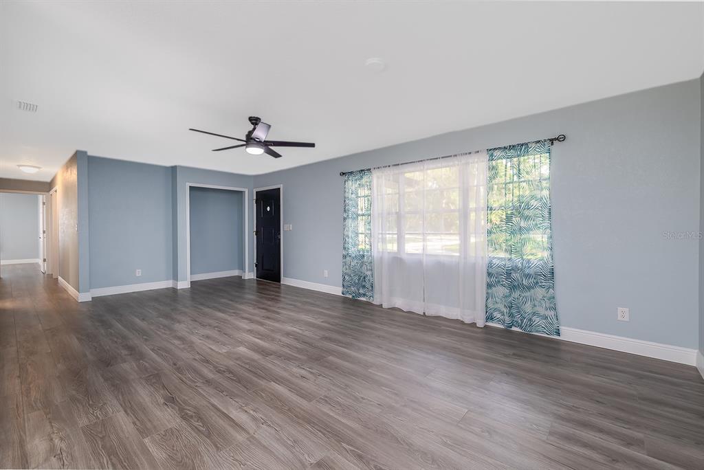 A living room with light blue walls, wood-look flooring, a ceiling fan, and a window — 764 REED CANAL ROAD, SOUTH DAYTONA, FL