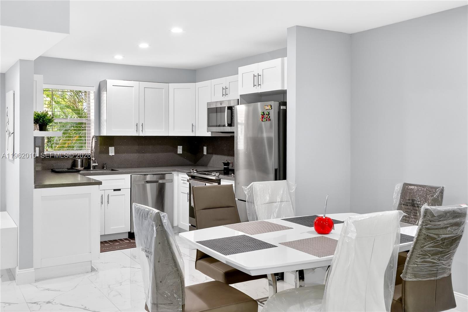 A kitchen with white cabinets and stainless steel appliances sits beside a dining area — 410 SE 2nd St # 111, Hallandale Beach FL 33009, HALLANDALE BEACH, FL