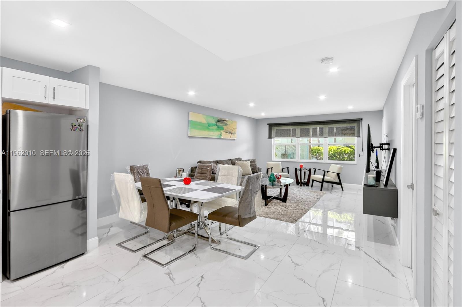 An open-concept living and dining area features white marble floors and a stainless steel refrigerator — 410 SE 2nd St # 111, Hallandale Beach FL 33009, HALLANDALE BEACH, FL