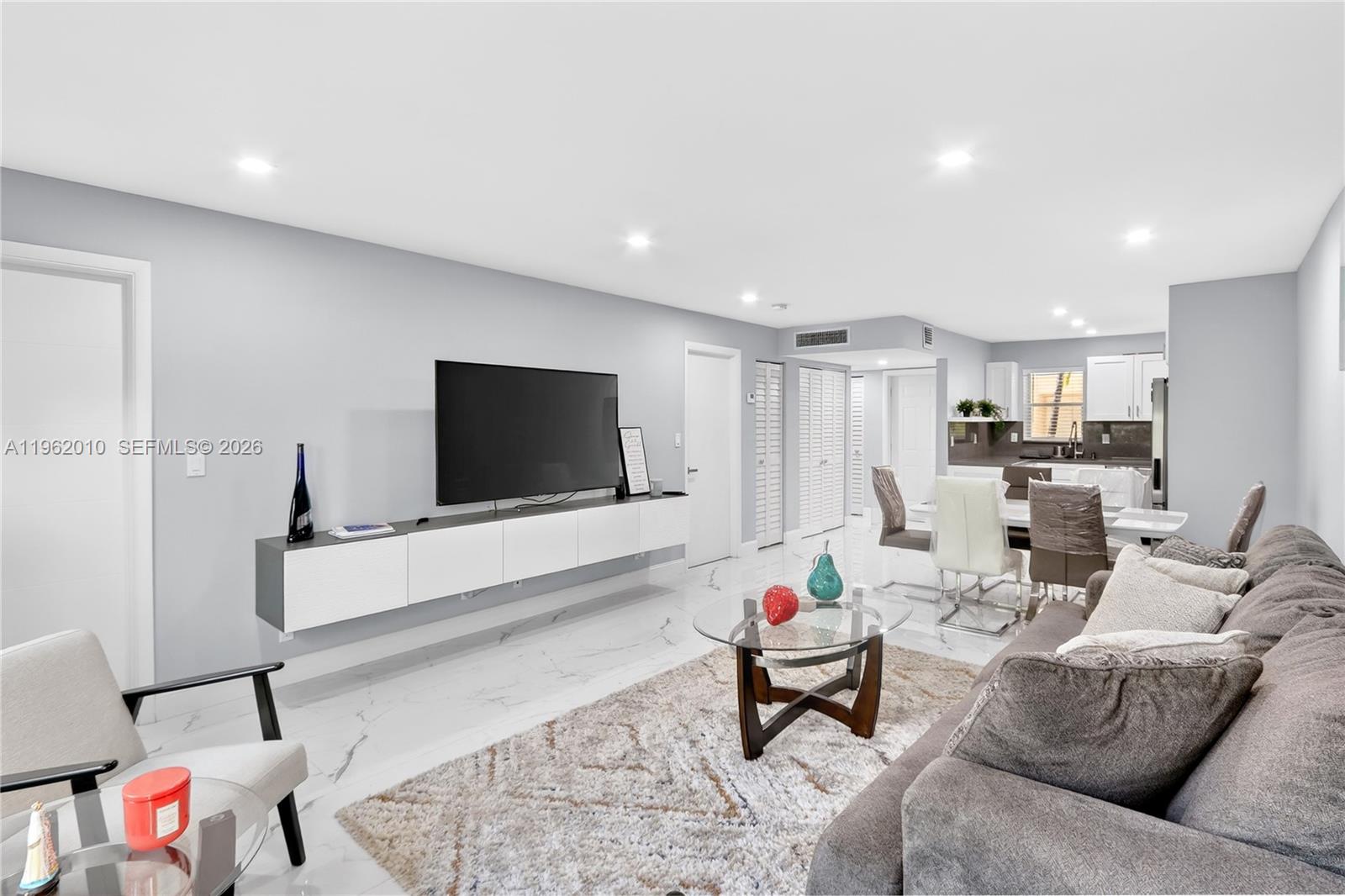 A living room features a floating media console, a grey sofa, and marble-style flooring — 410 SE 2nd St # 111, Hallandale Beach FL 33009, HALLANDALE BEACH, FL