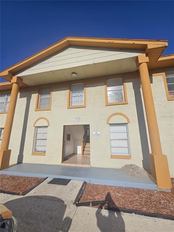 A two-story apartment building exterior features a tan brick facade, orange columns, and a gabled roof — 1709 MICHIGAN AVENUE UNIT C, KISSIMMEE, FL