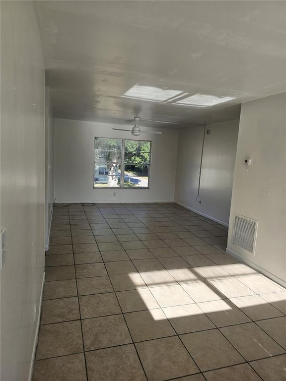 An empty room with beige tile flooring, a ceiling fan, and a large window — 1709 MICHIGAN AVENUE UNIT C, KISSIMMEE, FL