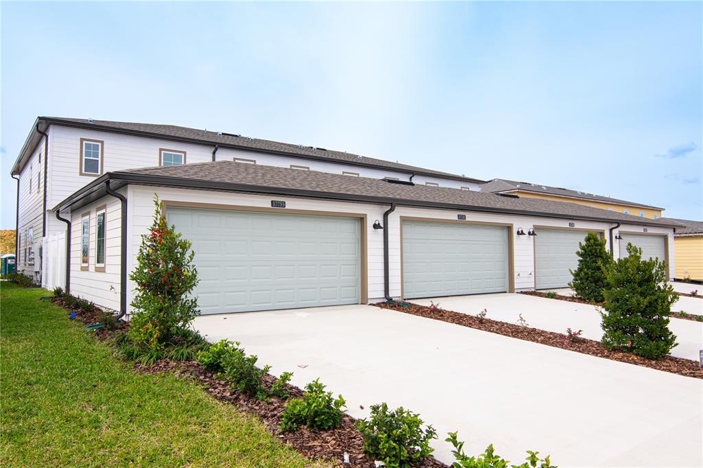 A row of townhouses with light green garage doors and white siding under a blue sky — 17741 JAPONICA BLOOM DRIVE, WINTER GARDEN, FL