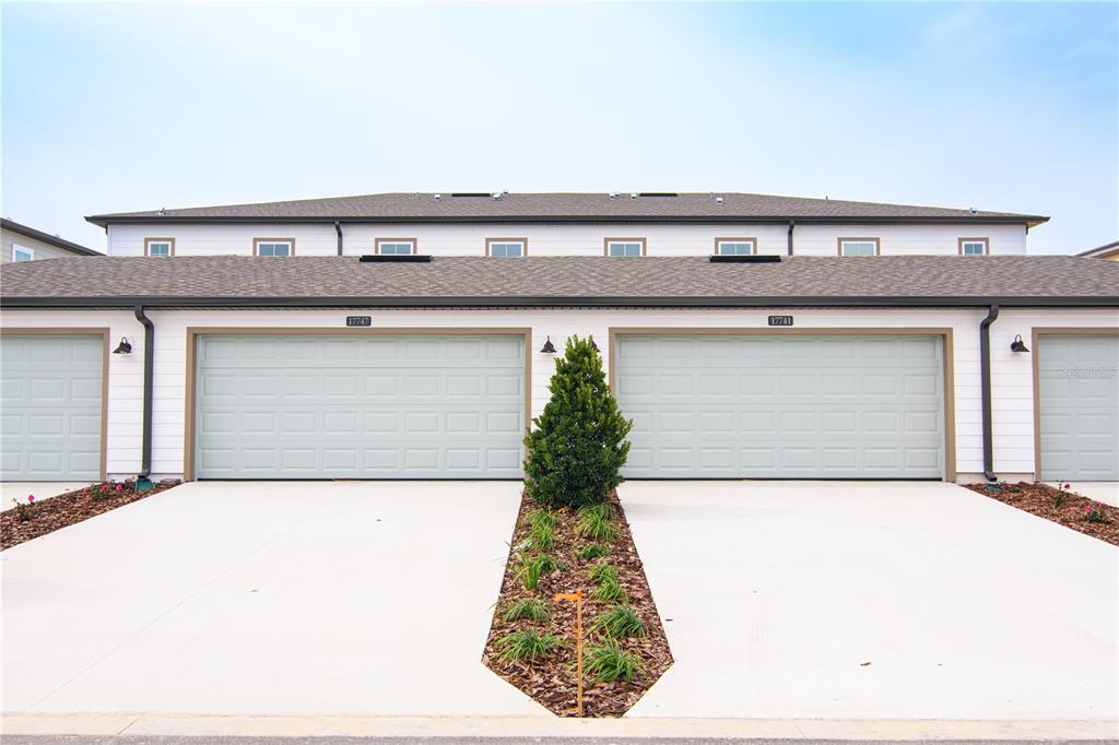 A two-story townhouse exterior with two garage doors and a central landscaped garden bed — 17741 JAPONICA BLOOM DRIVE, WINTER GARDEN, FL
