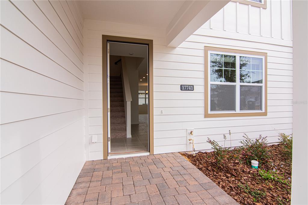 The exterior of a house features white horizontal siding, a brick walkway, and an open doorway — 17741 JAPONICA BLOOM DRIVE, WINTER GARDEN, FL