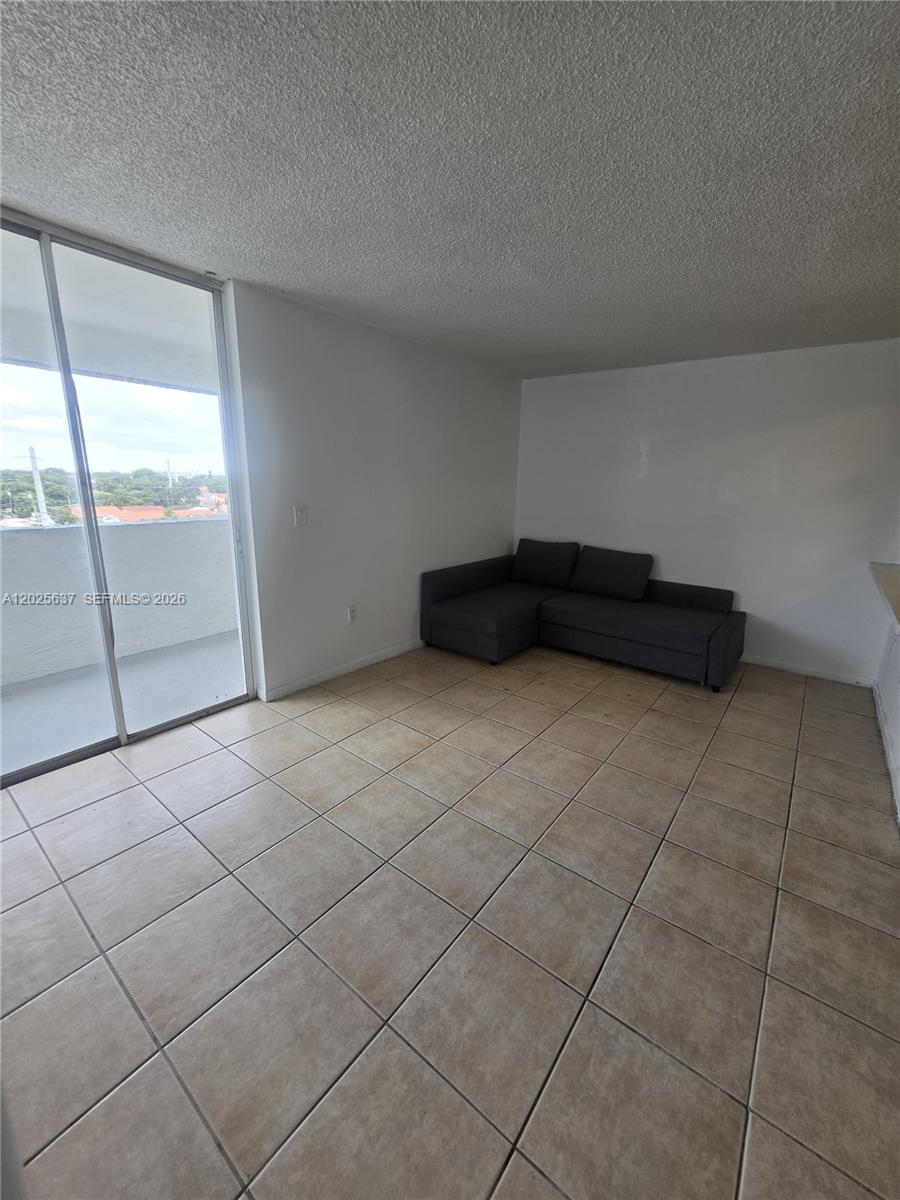 A living room features beige tile flooring, white walls, a gray sectional sofa, and sliding doors — 5050 NW 7th St # 610, Miami FL 33126, MIAMI, FL