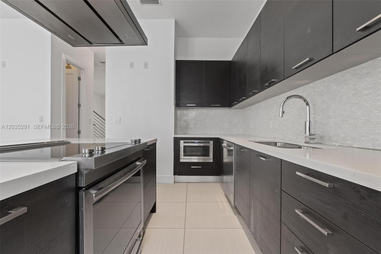 A modern kitchen features dark wood cabinetry, stainless steel appliances, and white countertops — 9161 NW 33rd St, Doral FL 33172, DORAL, FL