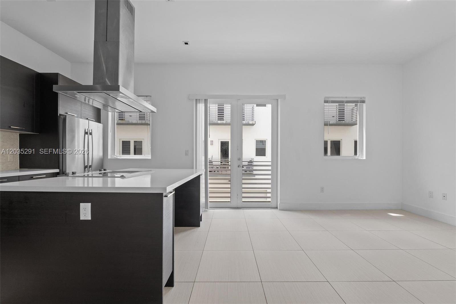 A modern kitchen with dark cabinets and a white island opens to a living area — 9161 NW 33rd St, Doral FL 33172, DORAL, FL