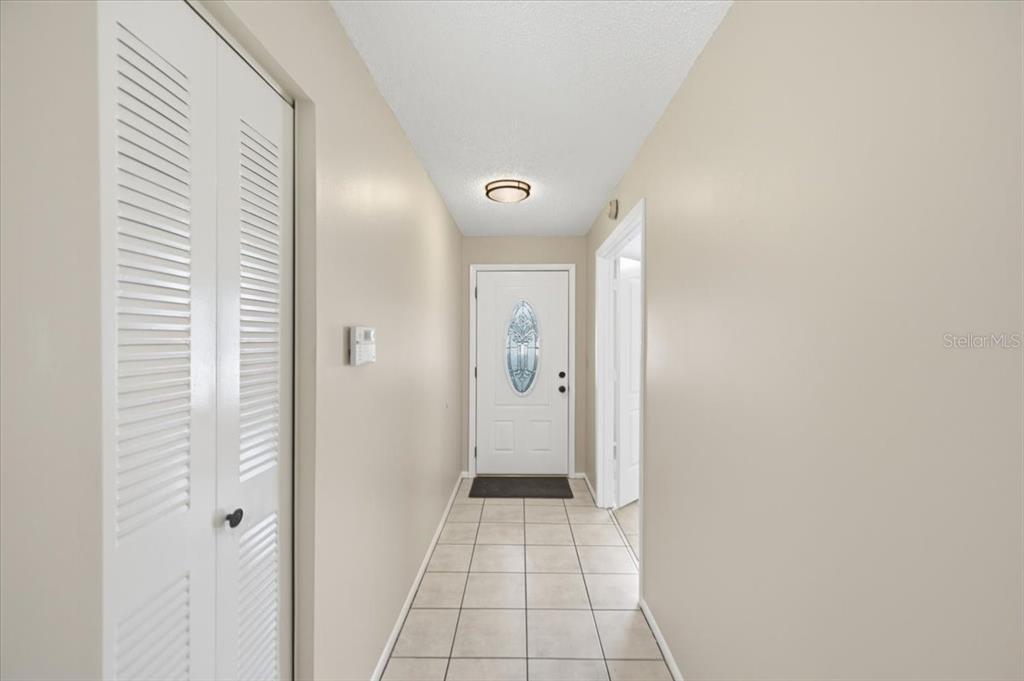 A tiled entryway features a white front door with a decorative glass insert and louvered closet — 1901 CASTLE BAY COURT, OLDSMAR, FL