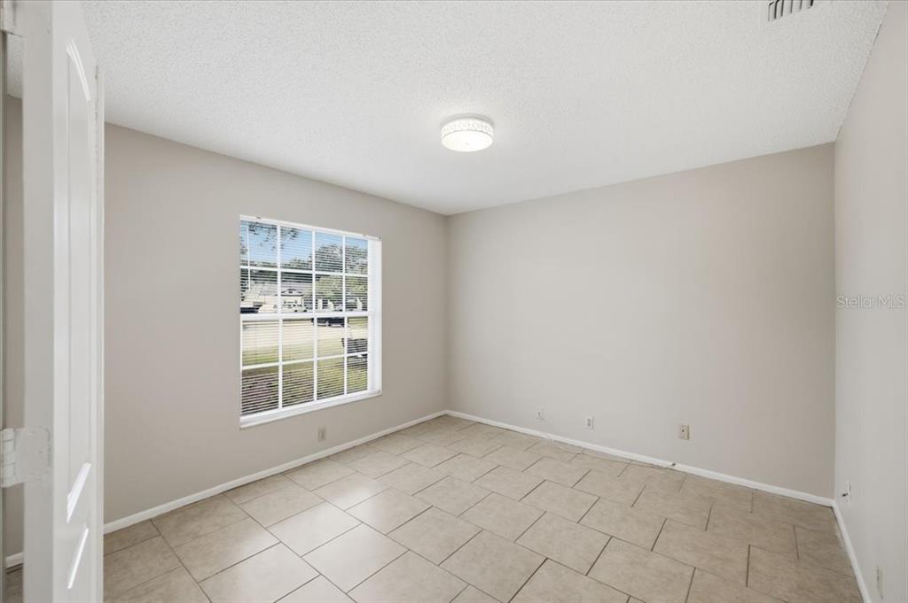 An empty room with beige walls, tile flooring, a single window, and a ceiling light — 1901 CASTLE BAY COURT, OLDSMAR, FL