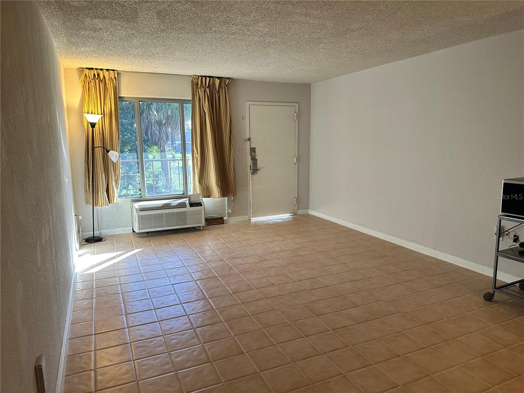 A living room features beige tile flooring, a window with gold curtains, and an entry door — 8421 S ORANGE BLOSSOM TRAIL UNIT 443, ORLANDO, FL