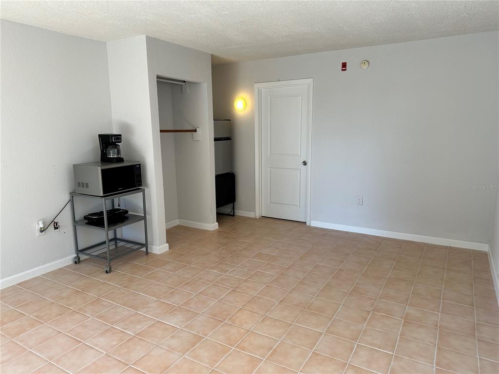 A room with light-colored walls, tiled flooring, a microwave cart, and a closed door — 8421 S ORANGE BLOSSOM TRAIL UNIT 443, ORLANDO, FL