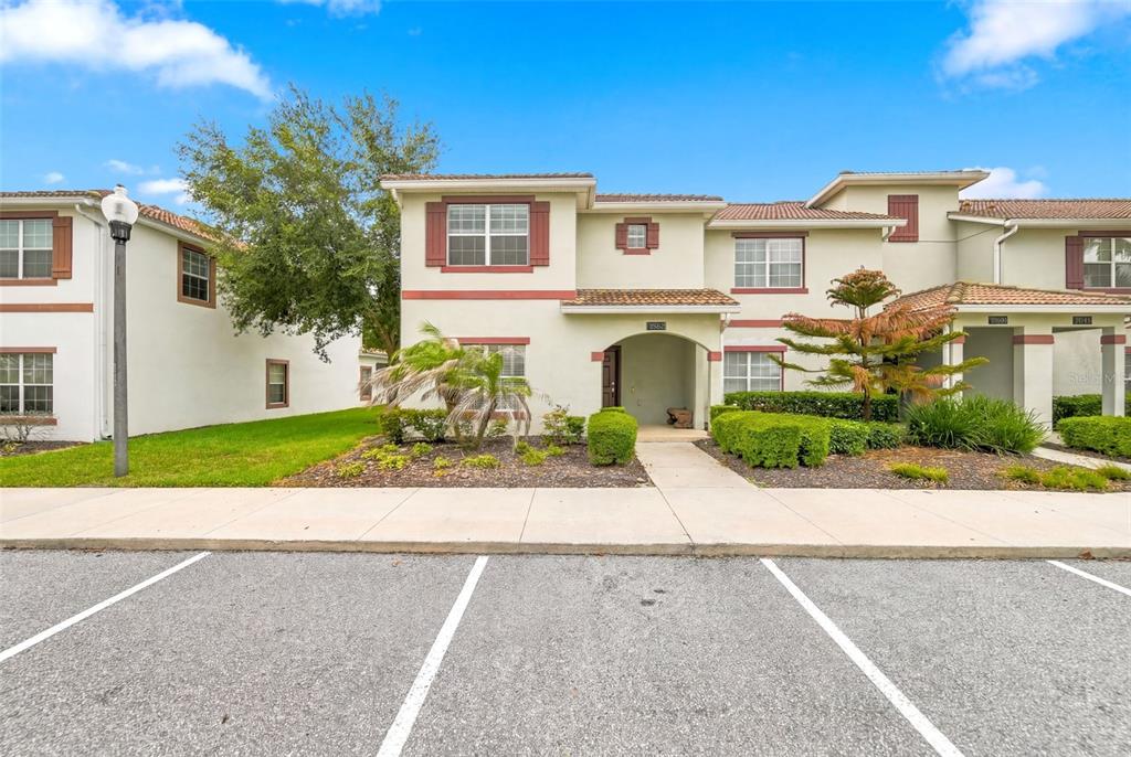 A two-story townhouse exterior with a tan stucco facade, red trim, and a paved parking area — 1582 MOON VALLEY DRIVE, DAVENPORT, FL