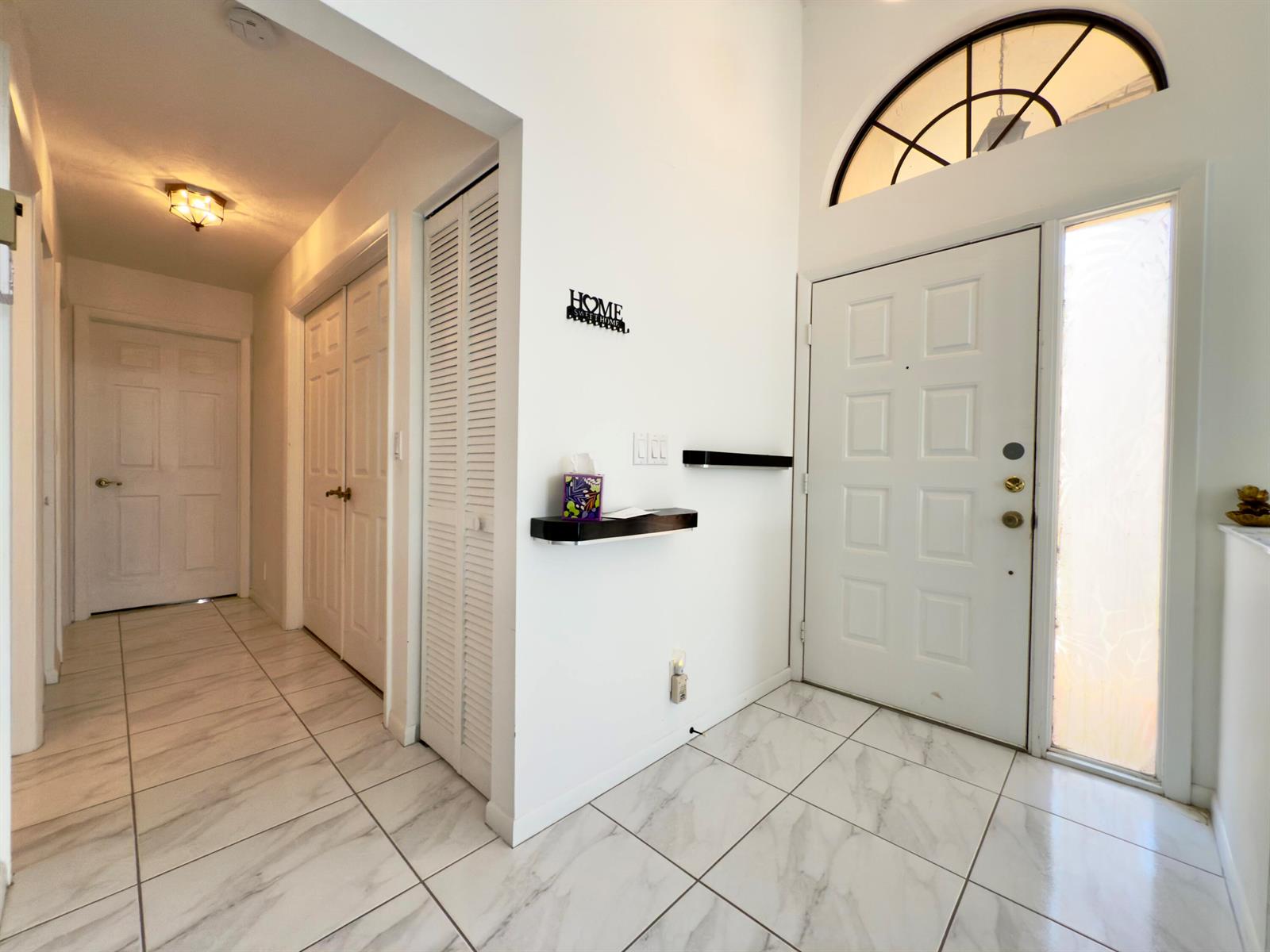 An entryway features white tiled floors, a front door with a transom window, and shelves — 8491 Heather Place, Boynton Beach FL 33472, BOYNTON BEACH, FL
