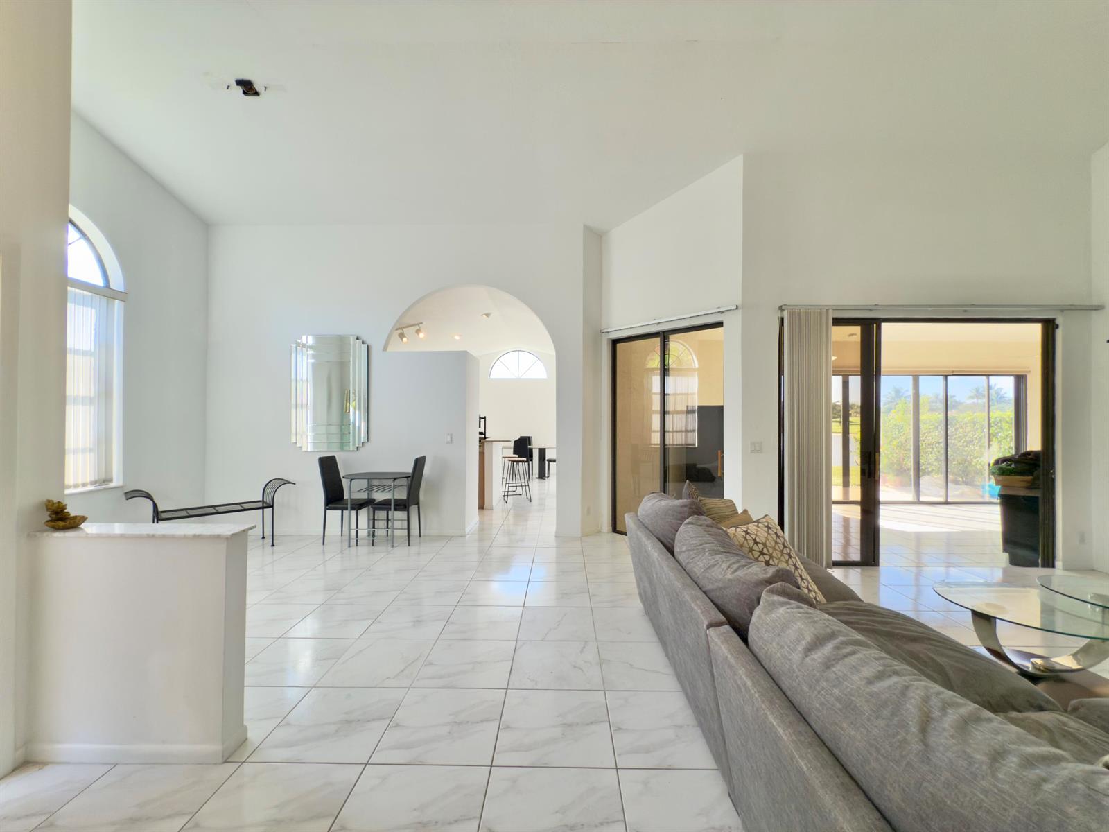 A bright living room features white marble-look tile floors, an arched entryway, and sliding glass doors — 8491 Heather Place, Boynton Beach FL 33472, BOYNTON BEACH, FL