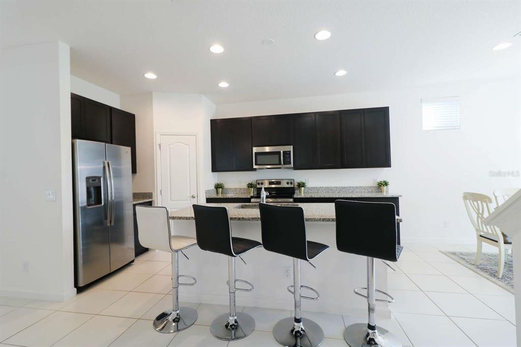 A kitchen with dark cabinets, stainless steel appliances, granite countertops, and a breakfast bar — 8016 SWEET ORANGE AVENUE, WINTER GARDEN, FL