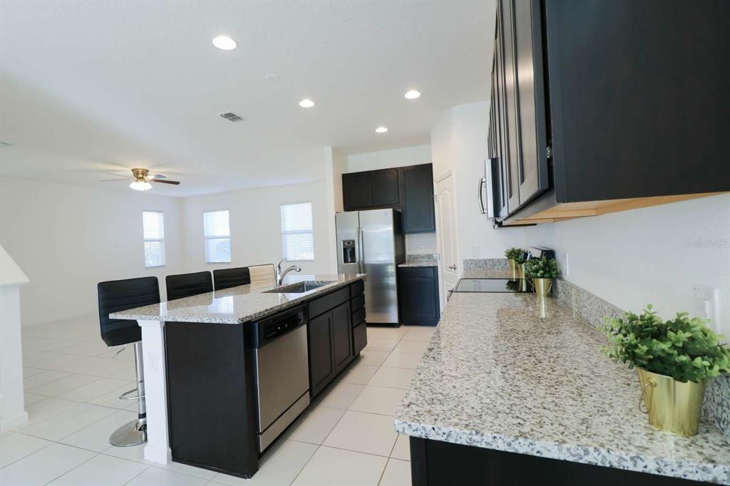 A kitchen features dark cabinets, granite countertops, a stainless steel refrigerator, and a breakfast bar — 8016 SWEET ORANGE AVENUE, WINTER GARDEN, FL