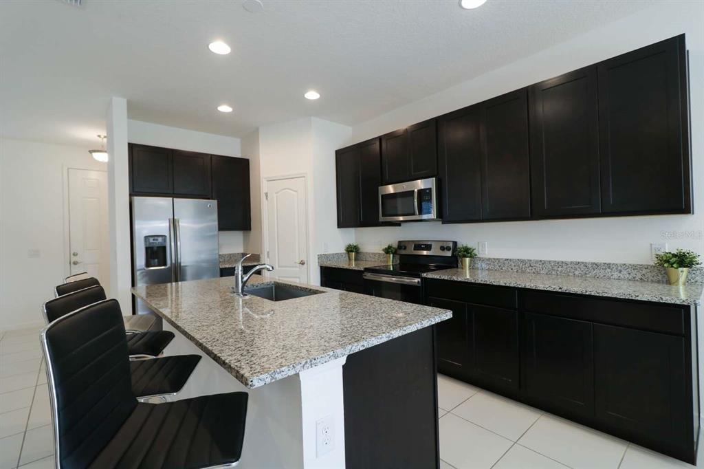 A kitchen features dark cabinetry, granite countertops, a stainless steel refrigerator, and a center island — 8016 SWEET ORANGE AVENUE, WINTER GARDEN, FL