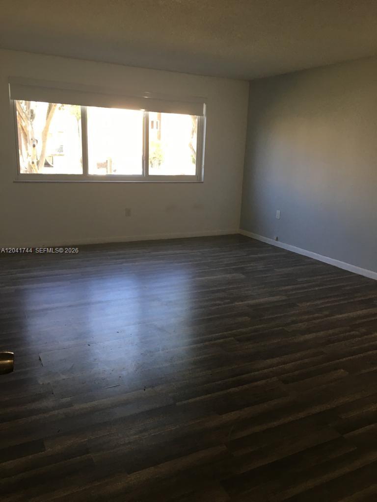 An empty room features dark wood-look flooring, light gray walls, and a large window — 6930 Miami Gardens Dr # 209, Hialeah FL 33015, HIALEAH, FL