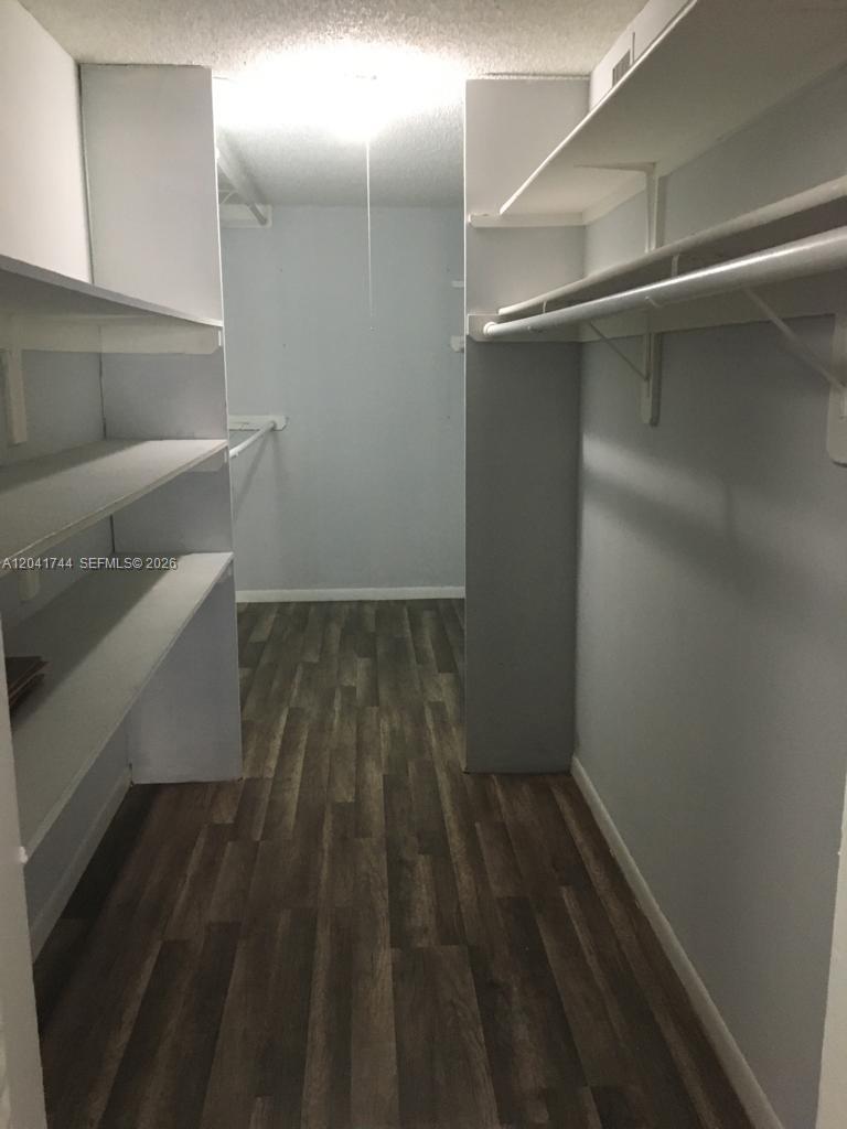 A walk-in closet features white shelving, hanging rods, and dark wood-look flooring — 6930 Miami Gardens Dr # 209, Hialeah FL 33015, HIALEAH, FL