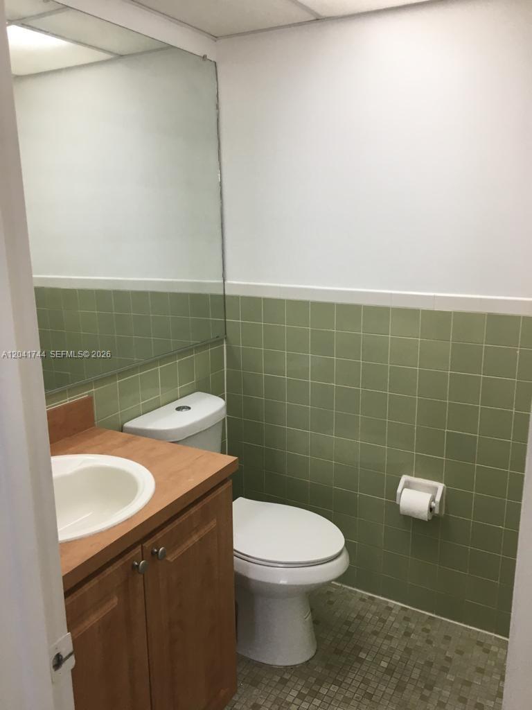 A bathroom features green wall tiles, a wood vanity, a white toilet, and a large mirror — 6930 Miami Gardens Dr # 209, Hialeah FL 33015, HIALEAH, FL