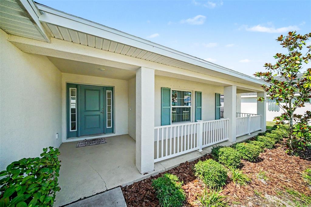 A covered front porch with a teal door, white railings, and a landscaped garden bed — 16253 VINE CLIFF AVENUE, HUDSON, FL