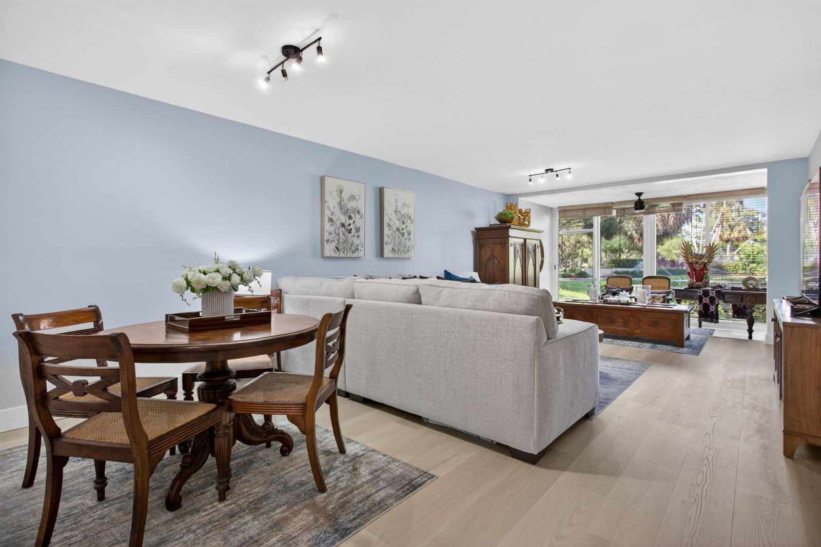 A dining area and living room with light blue walls, wood flooring, and large windows — 500 Oaks Lane # 111, Pompano Beach FL 33069, POMPANO BEACH, FL