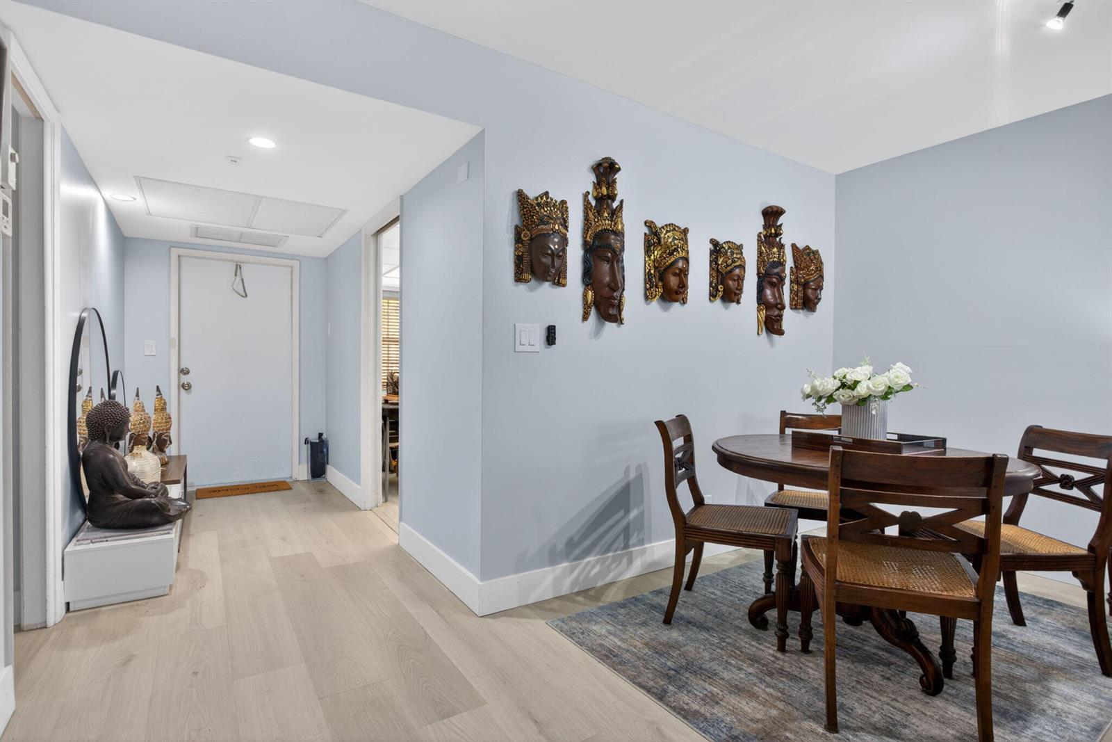 A dining area features a round wooden table, chairs, and decorative masks on a blue wall — 500 Oaks Lane # 111, Pompano Beach FL 33069, POMPANO BEACH, FL