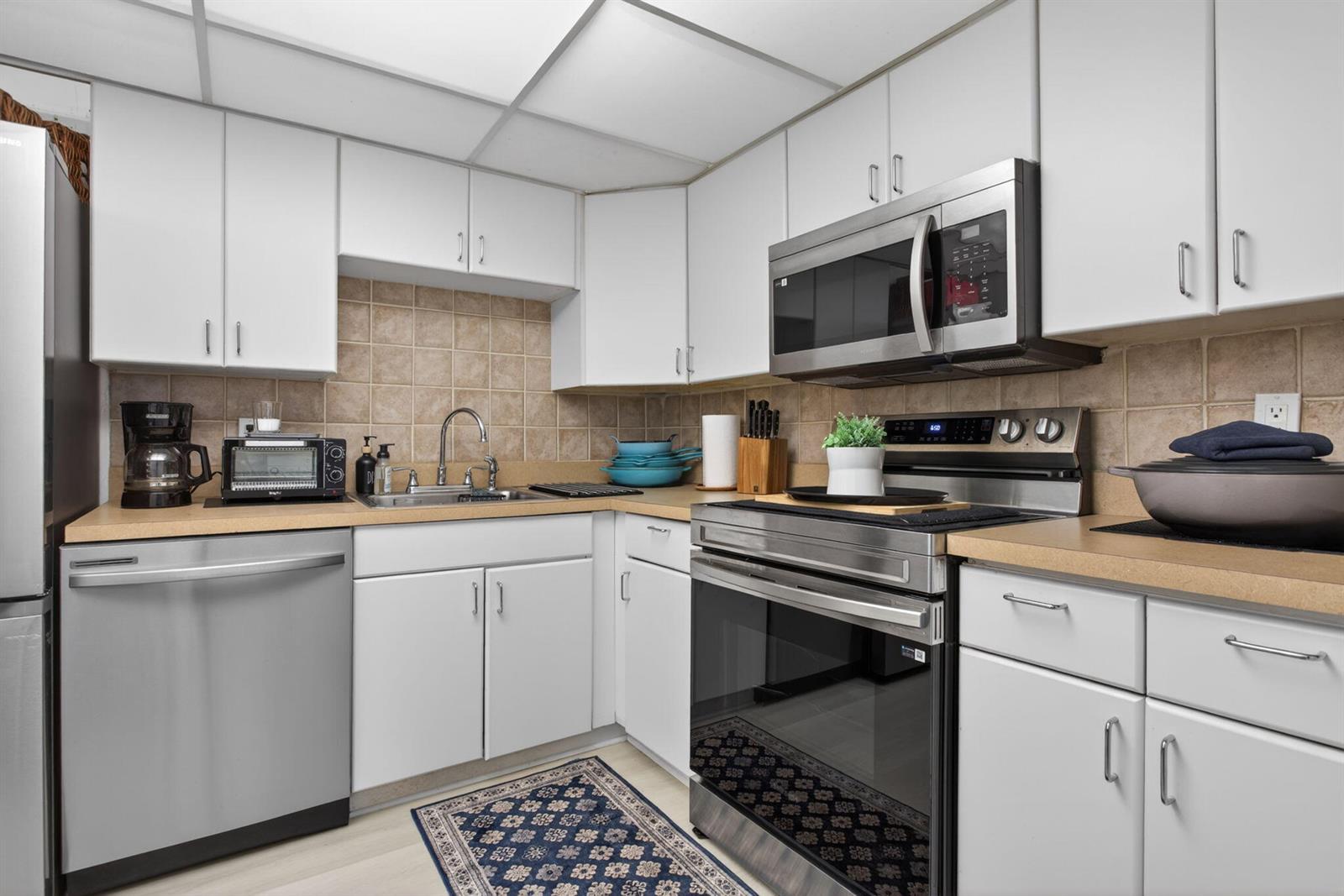 A kitchen features white cabinets, stainless steel appliances, tan countertops, and a tiled backsplash — 500 Oaks Lane # 111, Pompano Beach FL 33069, POMPANO BEACH, FL