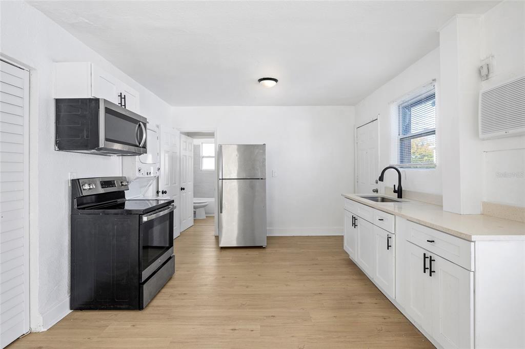 A kitchen features white cabinets, stainless steel appliances, a black stove, and light wood flooring — 1761 19TH STREET S, ST PETERSBURG, FL