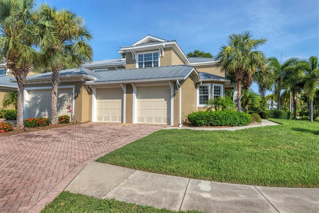 A two-story tan house with a metal roof, two garage doors, and palm trees — 10600 LEMON CREEK LOOP UNIT 104, ENGLEWOOD, FL