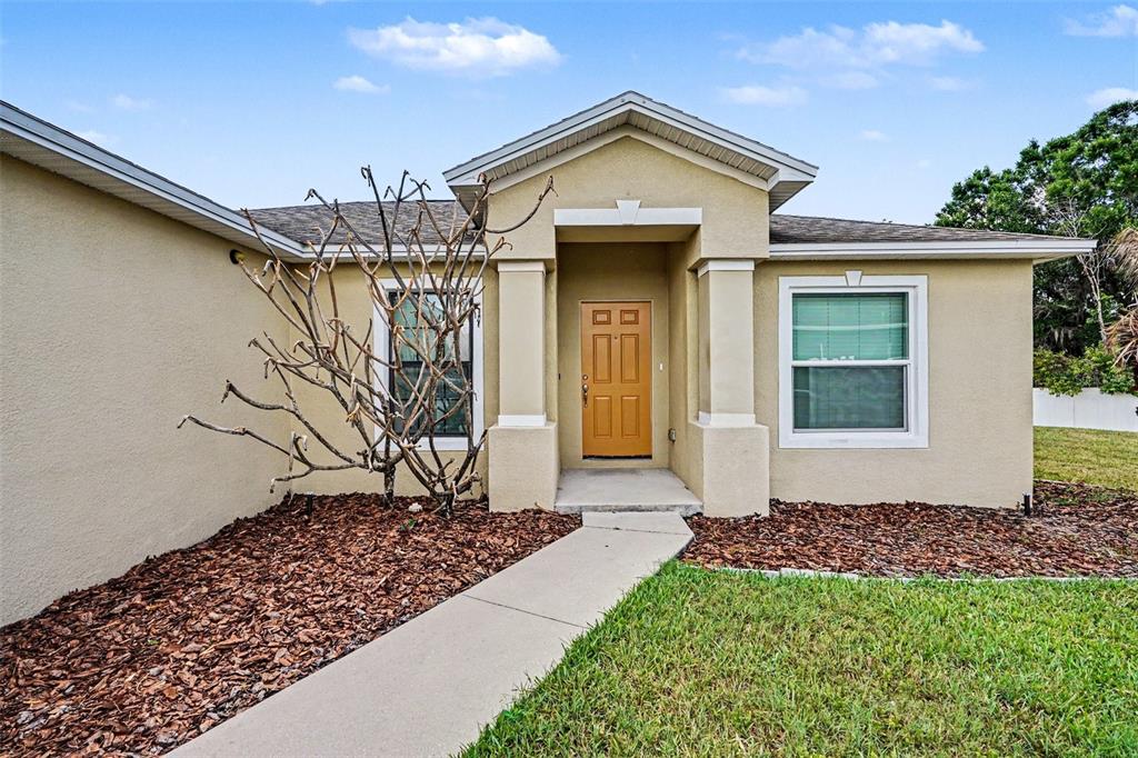 The exterior of a tan house features a front door, a walkway, and a bare tree — 8187 WOODVINE CIRCLE, LAKELAND, FL