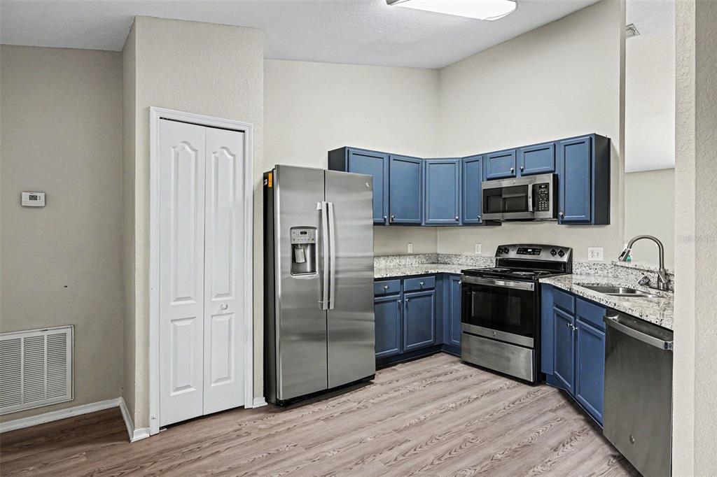A kitchen features blue cabinets, stainless steel appliances, granite countertops, and light wood-look flooring — 8187 WOODVINE CIRCLE, LAKELAND, FL