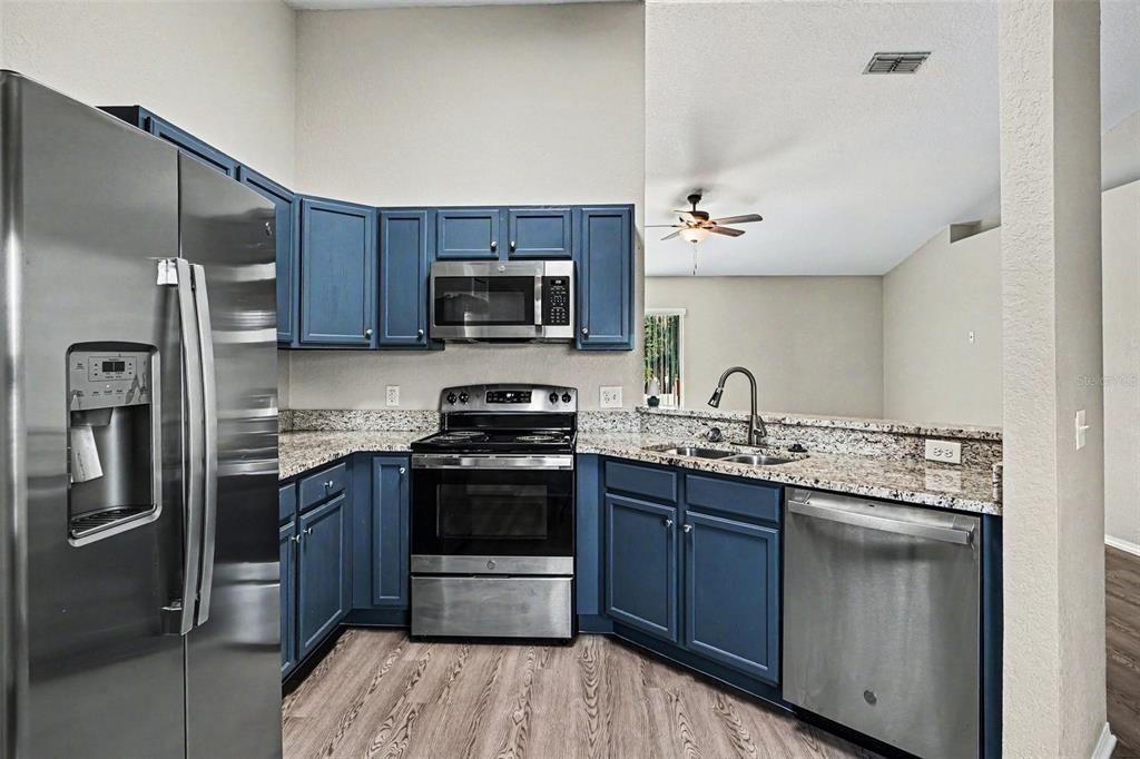 A kitchen features blue cabinets, granite countertops, stainless steel appliances, and wood-look flooring — 8187 WOODVINE CIRCLE, LAKELAND, FL