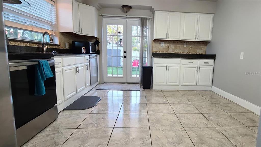A kitchen features white cabinets, dark countertops, tile flooring, and glass doors leading outside — 2306 W SAINT JOSEPH STREET, TAMPA, FL