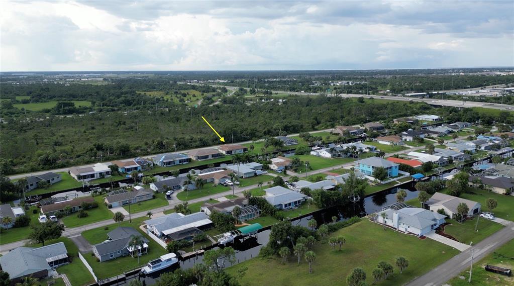 An aerial view shows a residential neighborhood with houses along a canal and a highway — 3103 RIVERSIDE DRIVE, PUNTA GORDA, FL