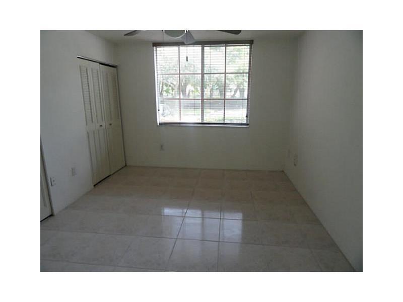 An empty room features light-colored tile flooring, white walls, a window with blinds, and closets — 12166 Saint Andrews Place # 111, Miramar FL 33025, MIRAMAR, FL