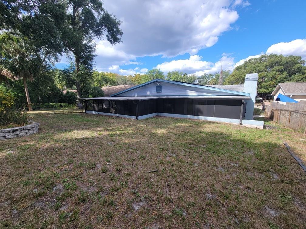 The backyard features a house with a large screened-in porch and a stone retaining wall — 11633 FOX RUN, PORT RICHEY, FL