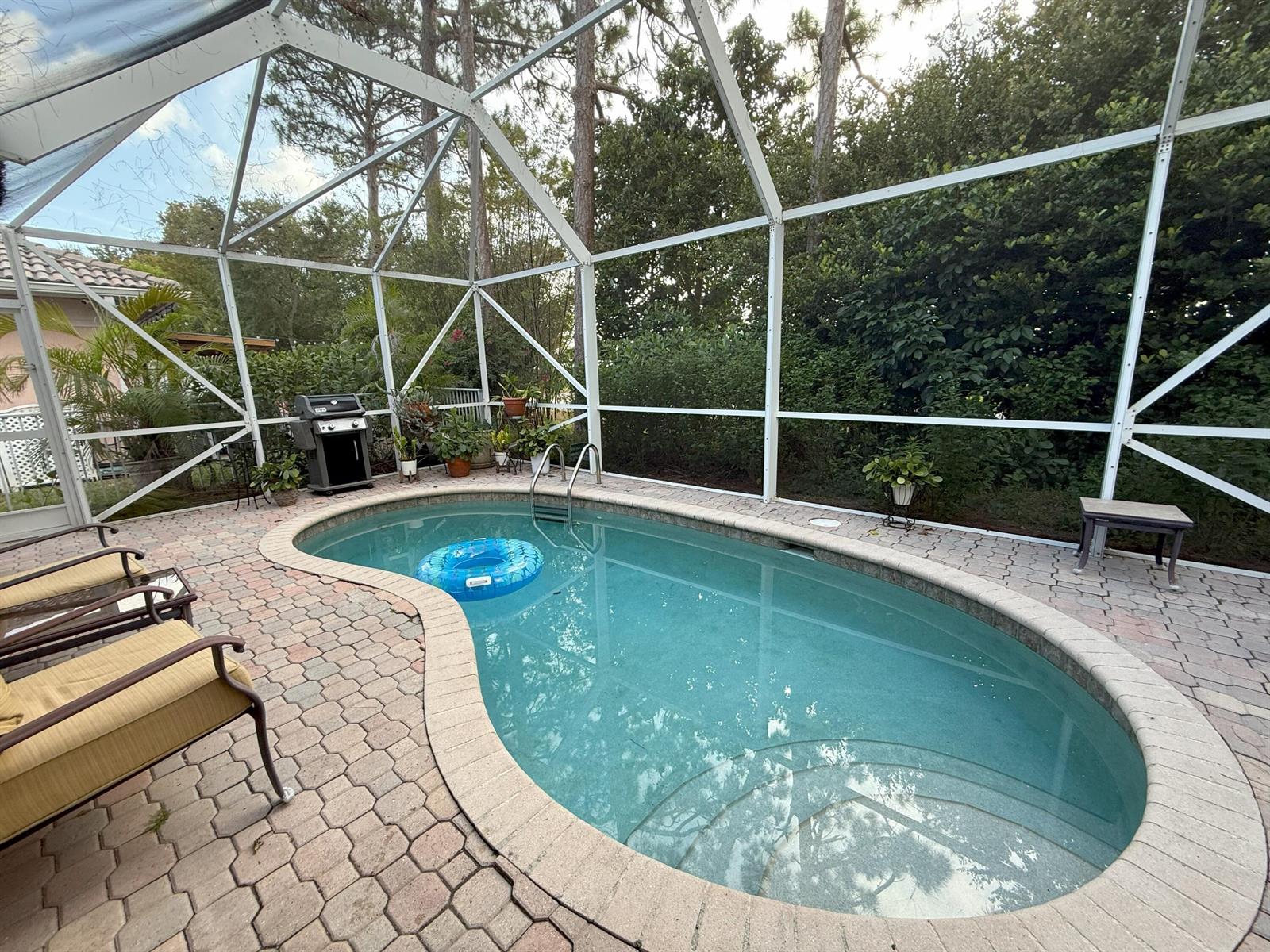 A screened-in patio features a kidney-shaped swimming pool, paver decking, and outdoor seating — 328 W Coral Trace Circle, Delray Beach FL 33445, DELRAY BEACH, FL