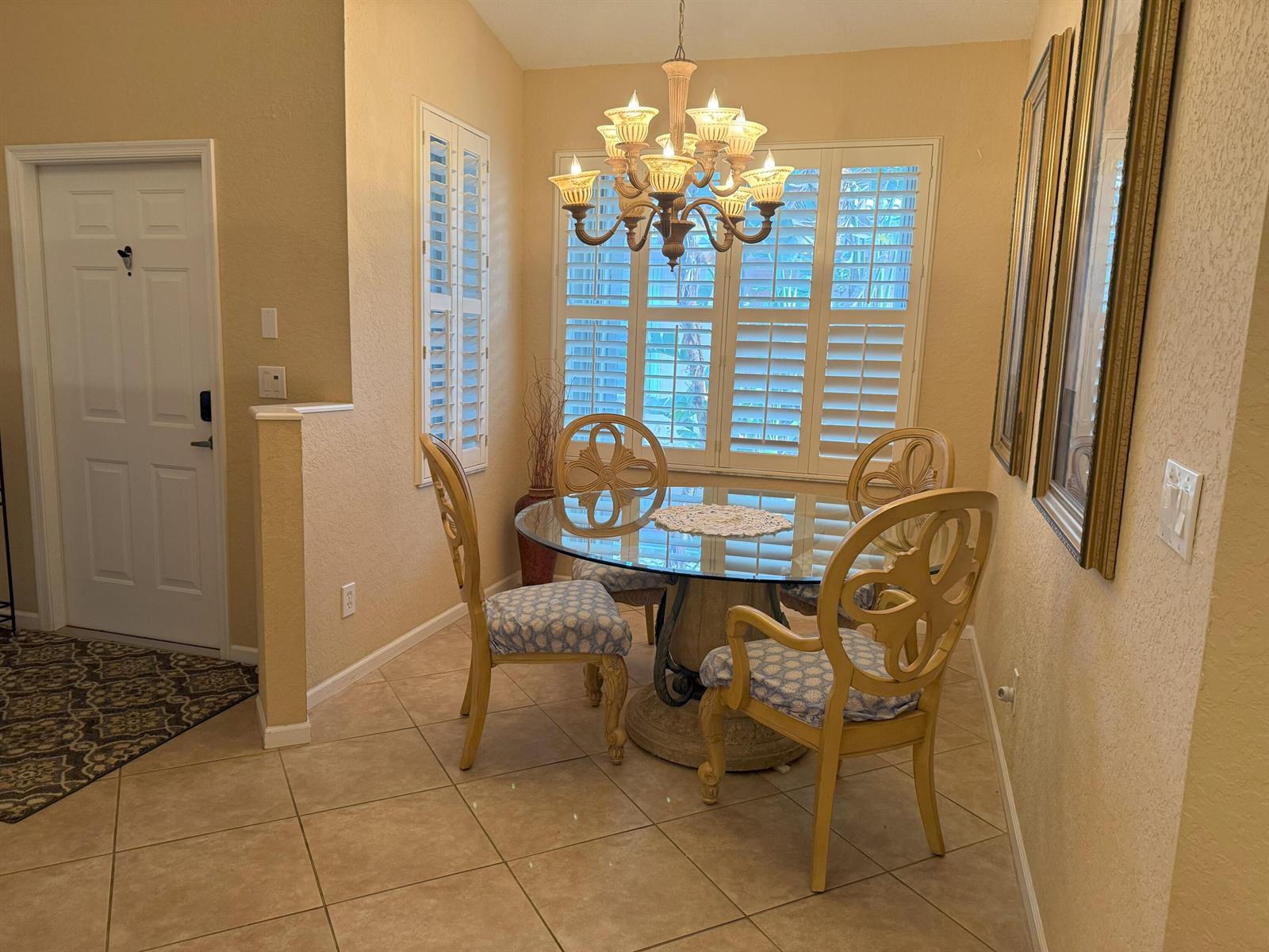 A dining area features a glass-topped table, four patterned chairs, and a chandelier under shutters — 328 W Coral Trace Circle, Delray Beach FL 33445, DELRAY BEACH, FL